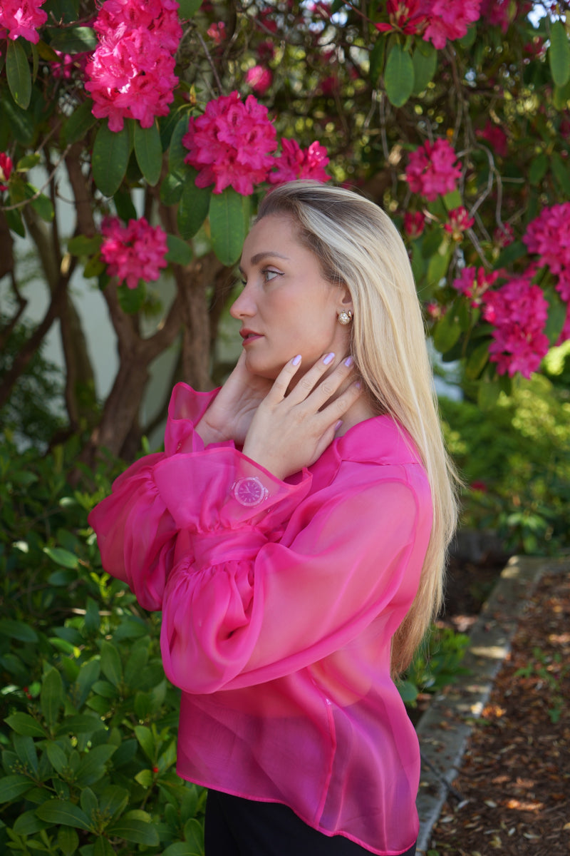 Seitenprofil einer blonden Frau in einer Seiden Organza Bluse von Lola Tong, im Hintergrund stehen Bäume mit pinken Blüten.