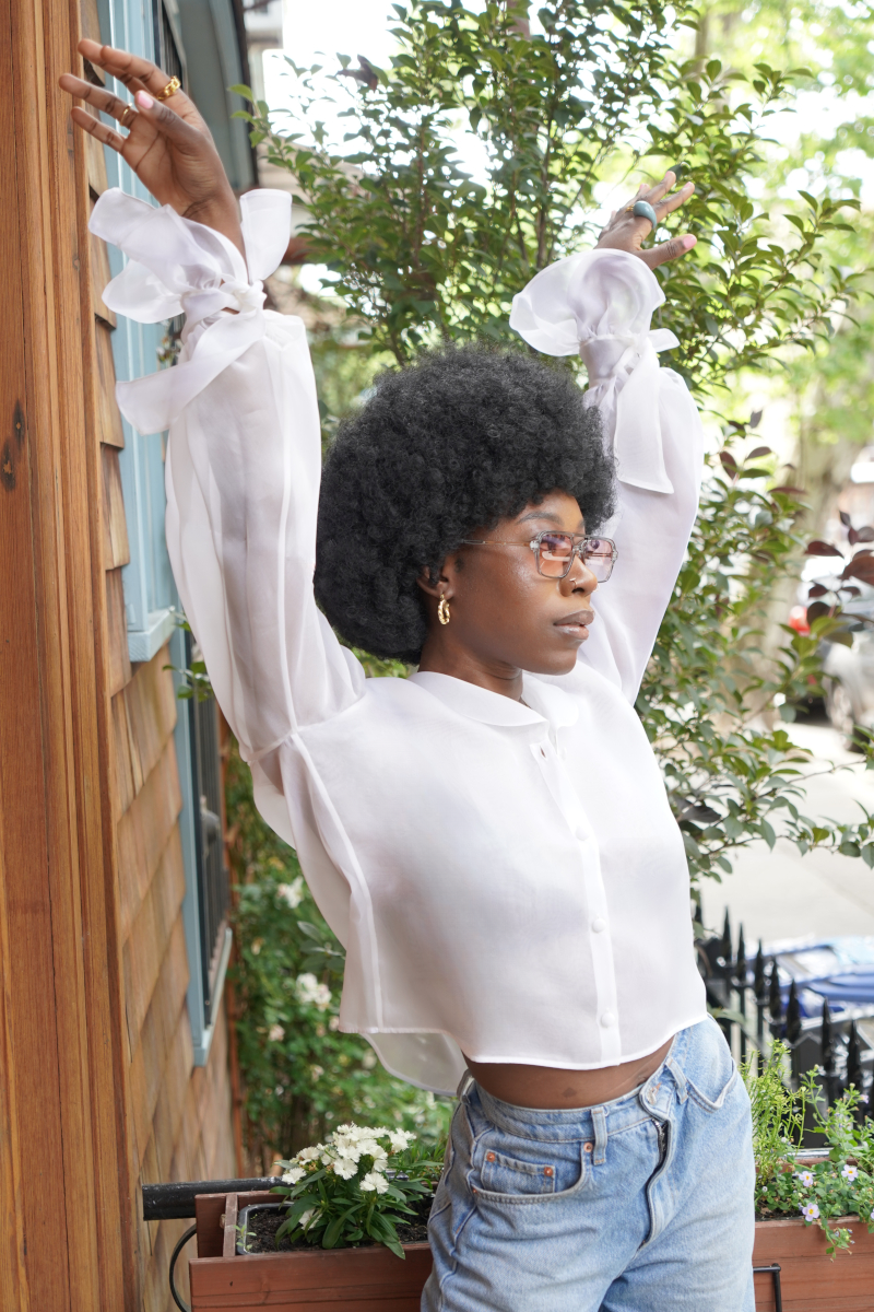 Young Afro-American women dancing in front of camera, her styling is blue jeans and a white silk organza blouse from Lola Tong and her hair is styled in a Afro.