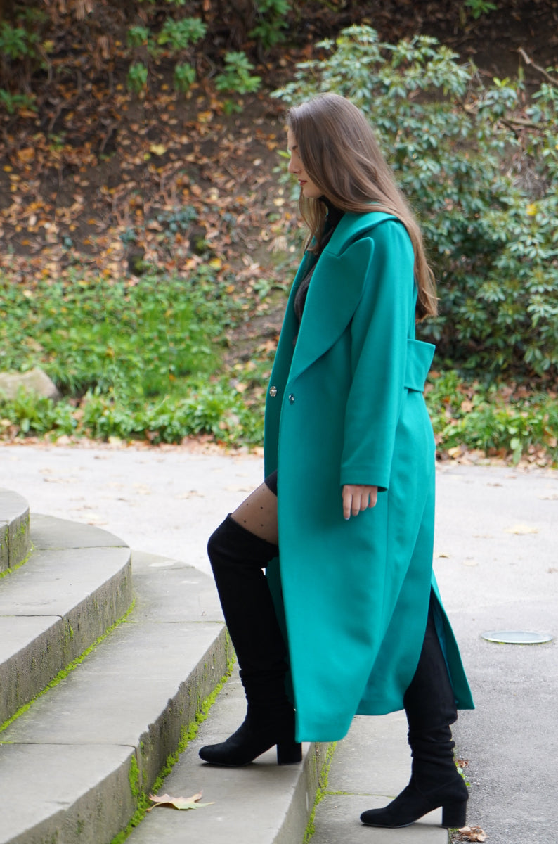 Eine junge Frau, die in Herbstmode, Wintermode einen langen grünen nachhaltigen Mantel aus Kaschmirwolle trägt und die Treppen steigt. 