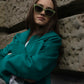 Eine junge Frau mit Sonnenbrille und einem grünen nachhaltigen Mantel von der Slow Fashion Brand Lola Tong. 