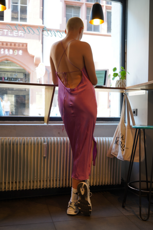 Rückenansicht einer Frau in einem rückenfreien rosa Seidenkleid von Lola Tong gestylt mit weissen Sneakers. 