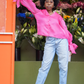 Eine junge modische Afro-Amerikanische Frau, die sich an einem Blumenladen anlehnt und gestylt ist in blauer Jeans und einer Seiden Organza Bluse in Hot Pink von Lola Tong und ihre Haare sind in einem wunderschönen Afro geschnitten.