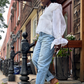 Eine junge Amerikanerin verlässt ihre Wohnung in einer blauen Jeans, der weißen Lola Tong-Bluse aus Seidenorganza und lindgrünen Absätzen. 