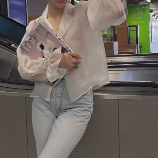junge Frau mit blonder Kurzhaarfrisur wartet an der Rolltreppe, in ihrer Hand die Deutsche Vogue und gestylt ist sie in blauer Jeans und einer weissen Bluse von Lola Tong. 
